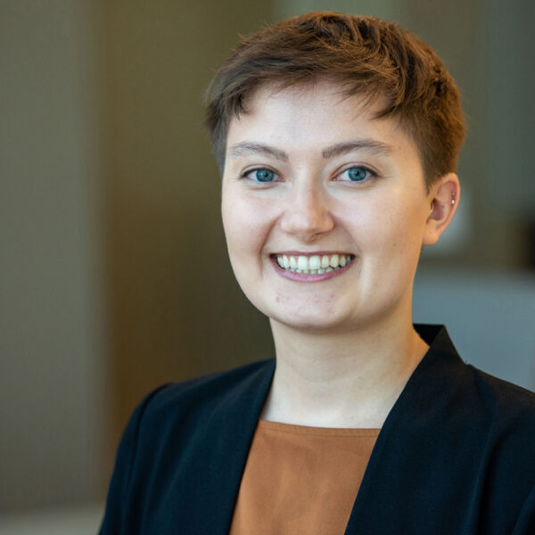 Portrait of Alaina Bottens smiling in a burnt orange top and black blazer.