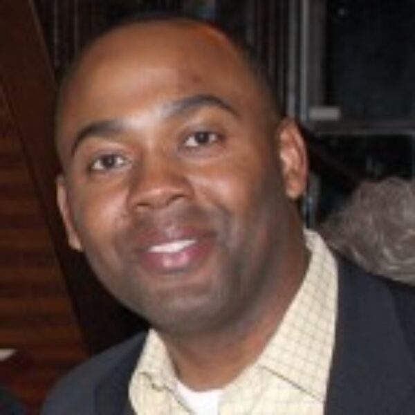 Portrait of Melvin Davis smiling in a cream checkered shirt and black blazer.